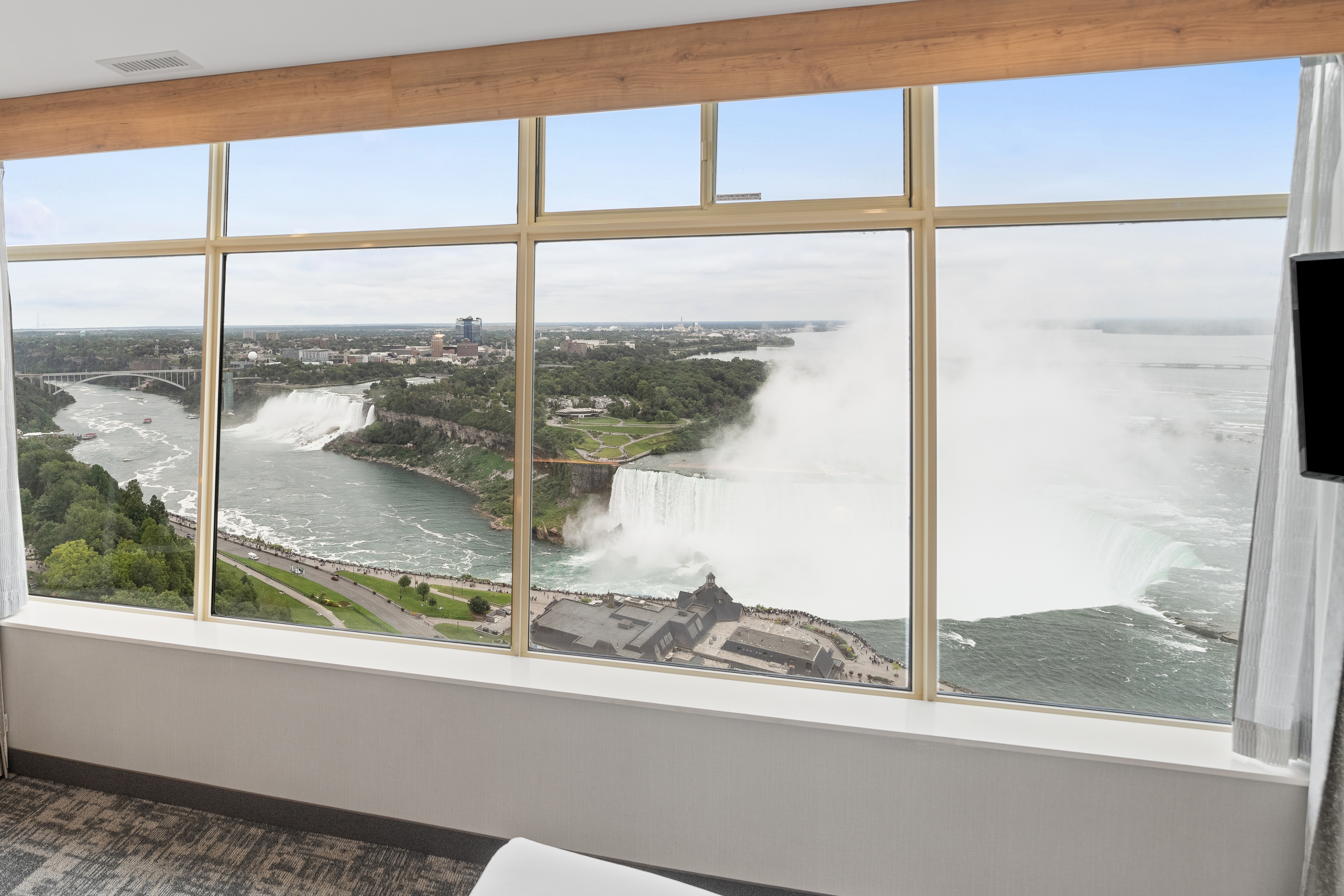 Hotel room with King Bed with white linens, expansive window offering scenic views of Niagara Falls