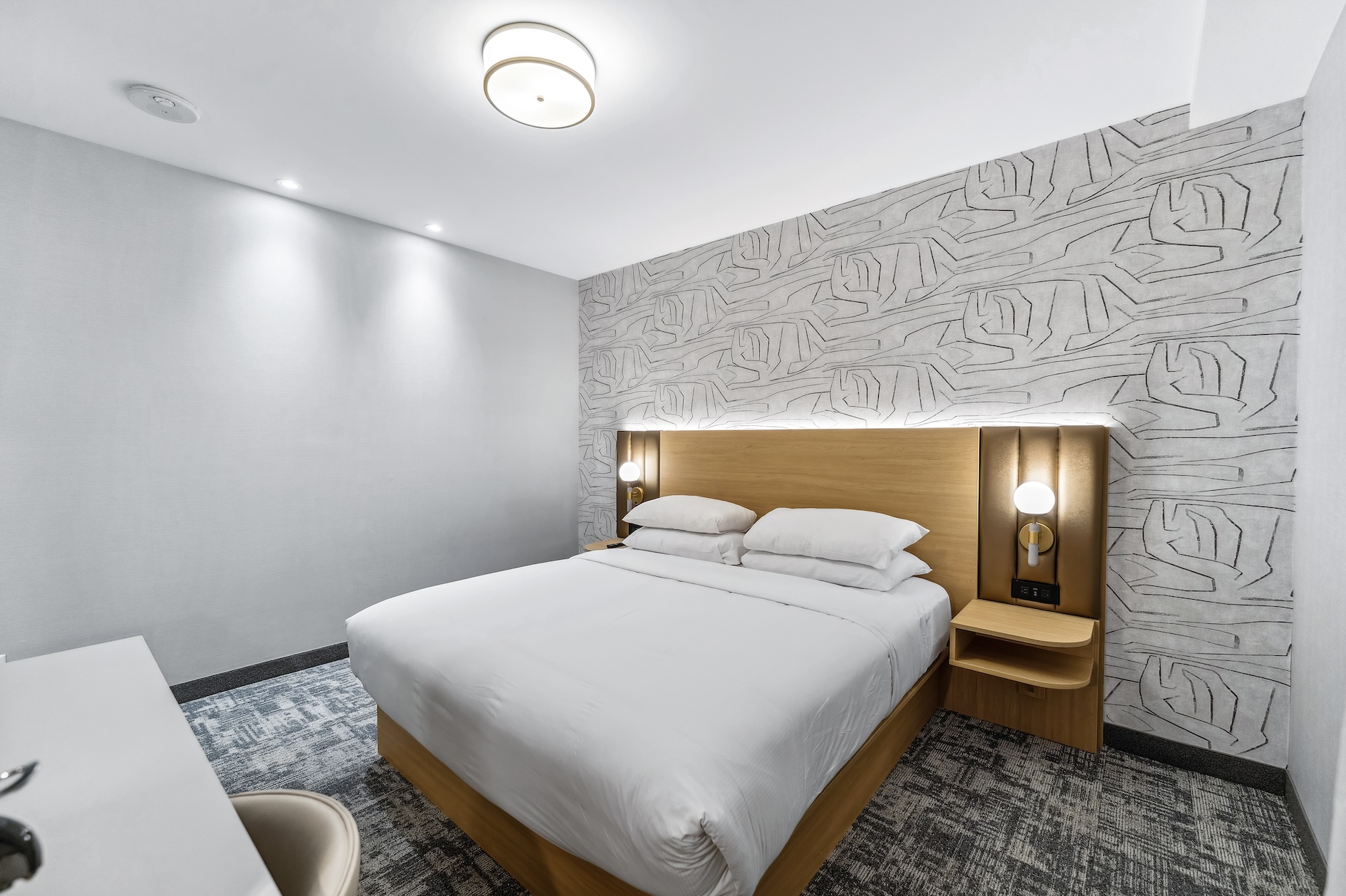 A hotel room with a king bed with white linen and a spacious desk for work or study purposes.