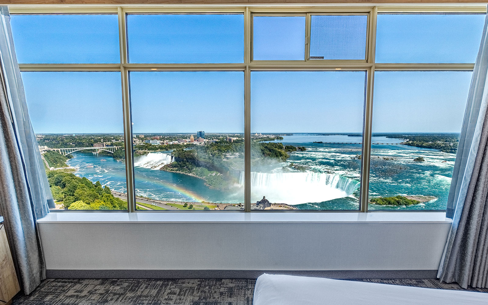 Hotel room with King Bed with white linens, expansive window offering scenic views of Niagara Falls